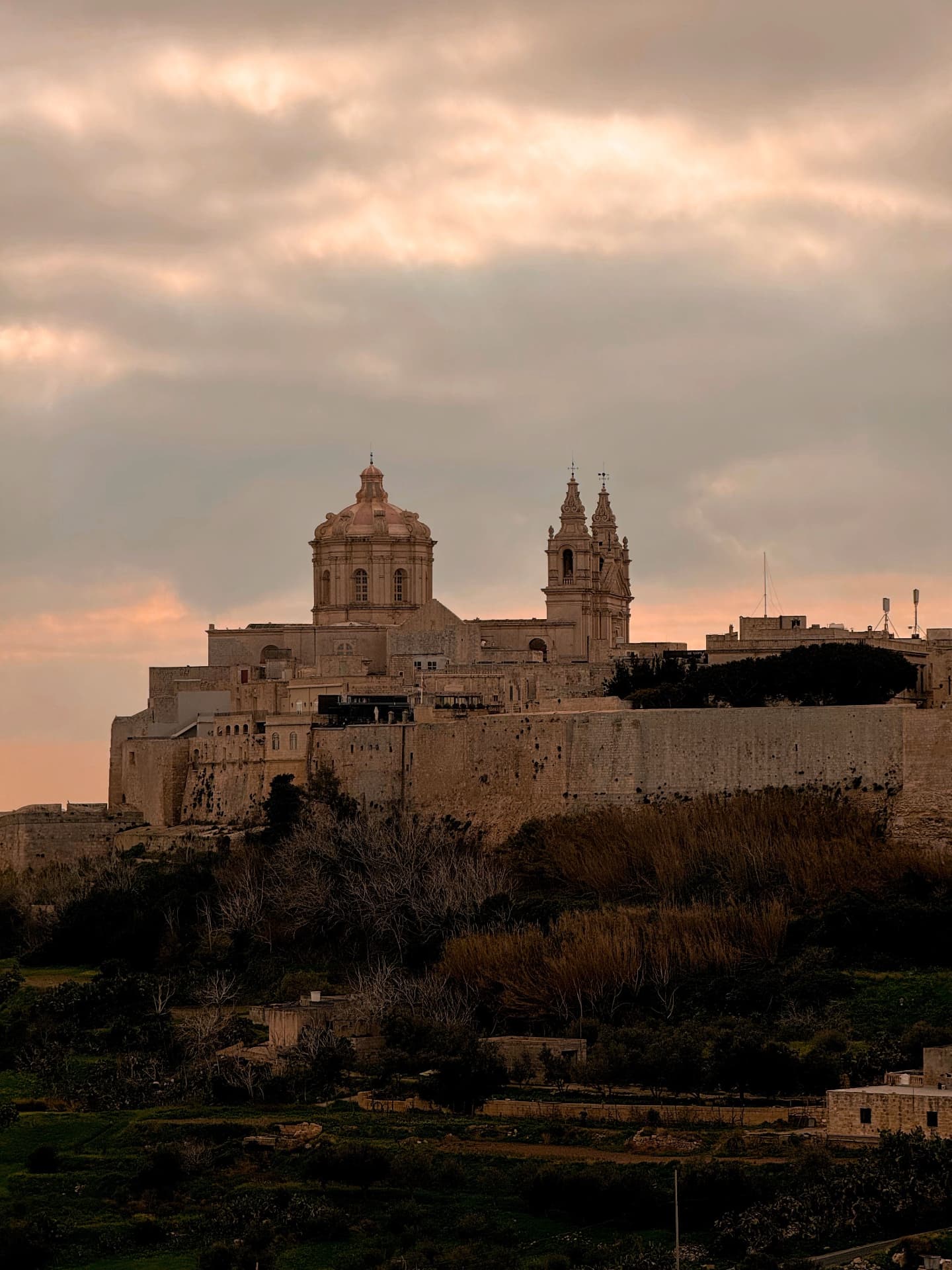 A fortified Maltese city beneath a warm evening sky
