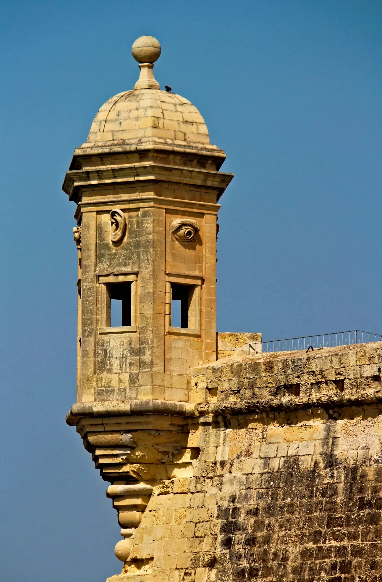 A historic Maltese watchtower with carved eyes and ears overlooking the sea